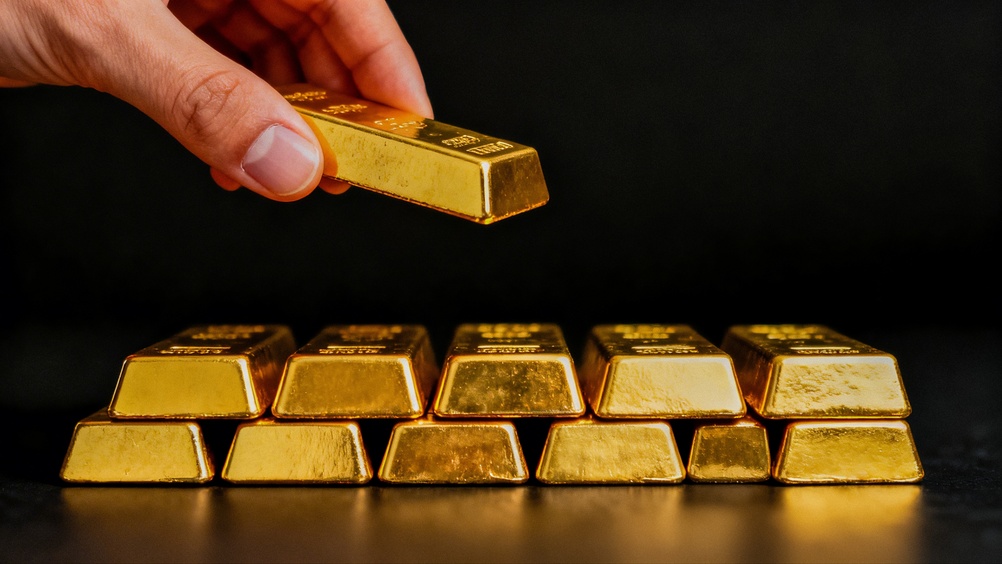 Hand,Holding,Gold,Bar,Over,Stack,Of,Gold,Bars,On